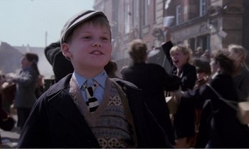 Movie still from “Hope and Glory” (1987), directed by John Boorman – A young boy wearing a hat and a tie; Medium shot, Low angle