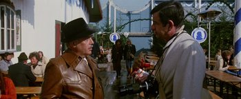 Movie still from “Hopscotch” (1980), directed by Ronald Neame – Two men are standing in a street talking to each other; Medium shot, Over the shoulder angle