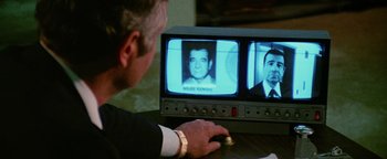 Movie still from “Hopscotch” (1980), directed by Ronald Neame – A man sitting in front of a tv with a picture on it; Extreme Close Up shot, Over the shoulder angle