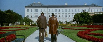 Movie still from “Hopscotch” (1980), directed by Ronald Neame – Two men are walking down a path in front of a white building; Wide shot, Low angle
