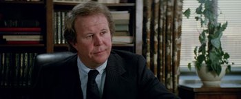 Movie still from “Hopscotch” (1980), directed by Ronald Neame – A man in a suit and tie sitting in front of a book shelf; Close Up shot, Over the shoulder angle