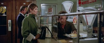 Movie still from “Hopscotch” (1980), directed by Ronald Neame – A man and a woman are standing behind a counter; Medium shot, Over the shoulder angle