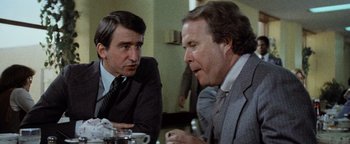 Movie still from “Hopscotch” (1980), directed by Ronald Neame – Two men in business suits sitting at a table talking to each other; Close Up shot, Over the shoulder angle