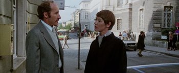 Movie still from “Hopscotch” (1980), directed by Ronald Neame – Two people standing on the sidewalk talking to each other; Medium shot, Low angle