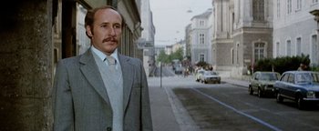 Movie still from “Hopscotch” (1980), directed by Ronald Neame – A man in a suit and tie standing on the side of the street; Medium shot, Low angle