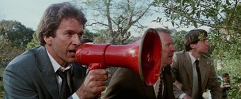 Movie still from “Hopscotch” (1980), directed by Ronald Neame – A man holding a red megaphone near another man; Medium shot, Low angle