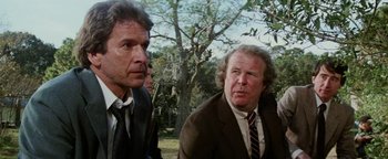 Movie still from “Hopscotch” (1980), directed by Ronald Neame – Two men in suits and ties standing next to each other in a park; Close Up shot, Low angle