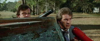 Movie still from “Hopscotch” (1980), directed by Ronald Neame – A man in a suit and tie holding a gun; Medium shot, Low angle