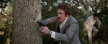 Movie still from “Hopscotch” (1980), directed by Ronald Neame – A man in a suit and tie holding a gun in his hand; Medium shot, Low angle