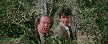 Movie still from “Hopscotch” (1980), directed by Ronald Neame – Two men standing next to each other near a bush; Close Up shot, Low angle