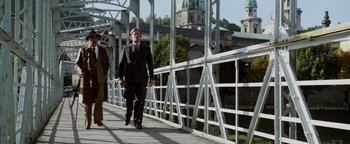Movie still from “Hopscotch” (1980), directed by Ronald Neame – A man in a suit and tie walking across a bridge; Wide shot, Low angle