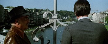 Movie still from “Hopscotch” (1980), directed by Ronald Neame – A man standing on a bridge over a river; Medium shot, Over the shoulder angle