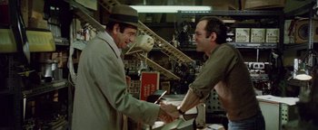 Movie still from “Hopscotch” (1980), directed by Ronald Neame – Two men shaking hands in an airplane shop; Medium shot, Over the shoulder angle