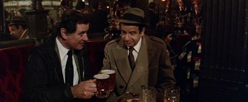 Movie still from “Hopscotch” (1980), directed by Ronald Neame – A man in a hat and a coat is holding a glass of beer; Medium shot, High angle