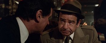 Movie still from “Hopscotch” (1980), directed by Ronald Neame – A man wearing a hat talking to another man in a suit; Close Up shot, Over the shoulder angle