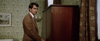 Movie still from “Hopscotch” (1980), directed by Ronald Neame – A man standing next to a wooden cabinet; Medium shot, Over the shoulder angle
