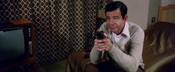 Movie still from “Hopscotch” (1980), directed by Ronald Neame – A man holding a cell phone while sitting on a couch; Medium shot, High angle