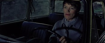 Movie still from “Hopscotch” (1980), directed by Ronald Neame – A woman sitting in the back seat of a car holding a steering wheel; Close Up shot, High angle