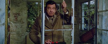 Movie still from “Hopscotch” (1980), directed by Ronald Neame – A man in a brown jacket is looking out of a window; Medium shot, Low angle