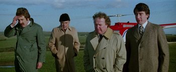 Movie still from “Hopscotch” (1980), directed by Ronald Neame – Two men standing next to each other on a field; Medium shot, Low angle