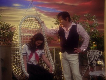Movie still from “House” (1977), directed by Nobuhiko Ôbayashi – A man and a woman are sitting on a swing; Medium shot, Low angle