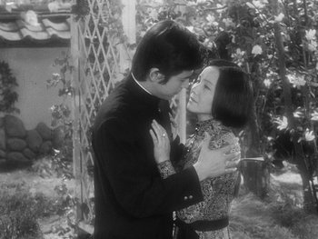 Movie still from “House” (1977), directed by Nobuhiko Ôbayashi – A man and a woman embracing each other in front of a wooden fence; Medium shot, High angle