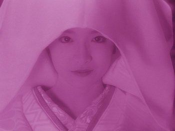 Movie still from “House” (1977), directed by Nobuhiko Ôbayashi – A woman in a white kimono is under a pink blanket; Close Up shot, High angle