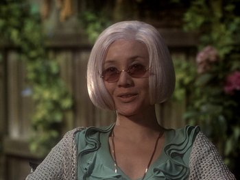 Movie still from “House” (1977), directed by Nobuhiko Ôbayashi – A woman with white hair wearing sunglasses and a green dress; Close Up shot, Over the shoulder angle