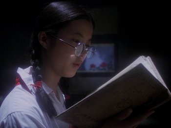Movie still from “House” (1977), directed by Nobuhiko Ôbayashi – A girl in glasses is reading a book in a dark room; Close Up shot, Low angle