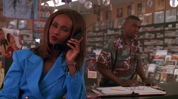 Movie still from “House Party 2” (1991), directed by Doug McHenry – A woman talking on a cell phone in front of a man; Medium shot, Low angle