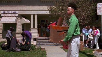 Movie still from “House Party 2” (1991), directed by Doug McHenry – A man holding a box in front of a house; Wide shot, High angle