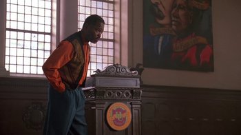 Movie still from “House Party 2” (1991), directed by Doug McHenry – A man standing in front of a podium in front of a window; Medium shot, Low angle