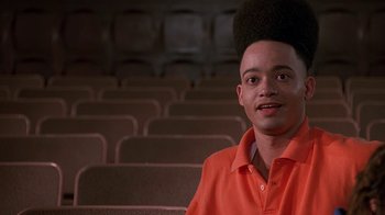 Movie still from “House Party 2” (1991), directed by Doug McHenry – A man in an orange shirt sitting in front of rows of seats; Close Up shot, Low angle