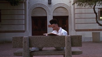 Movie still from “House Party 2” (1991), directed by Doug McHenry – A man sitting on top of a bench reading a book; Wide shot, High angle