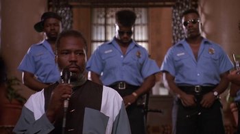 Movie still from “House Party 2” (1991), directed by Doug McHenry – A man holding a microphone in front of a group of men; Medium shot, Low angle