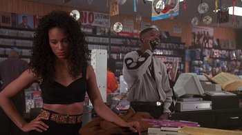 Movie still from “House Party 2” (1991), directed by Doug McHenry – A man talking on a phone while a woman stands behind him; Medium shot, Over the shoulder angle