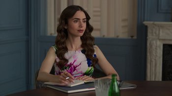 Movie still from “Emily in Paris” (2020), created by Darren Star – A woman sitting at a table writing in a notebook; Medium shot, Over the shoulder angle