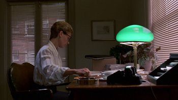 Movie still from “House of Games” (1987), directed by David Mamet – A man sitting at a desk in front of a laptop; Medium shot, Low angle