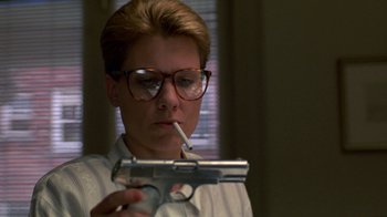 Movie still from “House of Games” (1987), directed by David Mamet – A woman smoking a cigarette while holding a gun; Close Up shot, Low angle