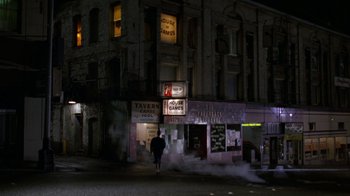 Movie still from “House of Games” (1987), directed by David Mamet – A person walking down the street in front of a building at night; Extreme Wide shot, High angle