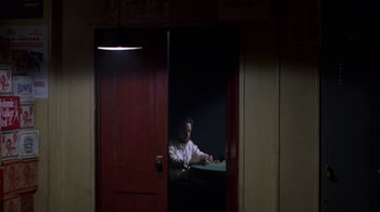 Movie still from “House of Games” (1987), directed by David Mamet – A man sitting at a table in a room; Wide shot, High angle