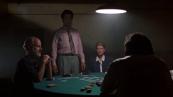 Movie still from “House of Games” (1987), directed by David Mamet – A group of people sitting around a table with cards on top of it; Medium shot, Over the shoulder angle