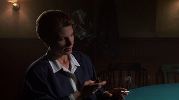 Movie still from “House of Games” (1987), directed by David Mamet – A woman smoking a cigarette while holding a cigarette holder; Close Up shot, Over the shoulder angle