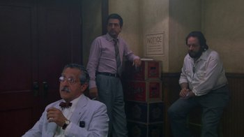 Movie still from “House of Games” (1987), directed by David Mamet – A group of men standing next to each other in a room; Wide shot, Low angle