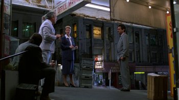 Movie still from “House of Games” (1987), directed by David Mamet – A group of people standing in front of a building; Wide shot, High angle