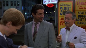 Movie still from “House of Games” (1987), directed by David Mamet – A man in a suit and tie standing next to another man in a suit and tie; Medium shot, Over the shoulder angle