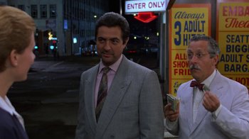 Movie still from “House of Games” (1987), directed by David Mamet – A man standing next to another man holding money; Medium shot, Over the shoulder angle