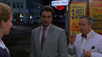 Movie still from “House of Games” (1987), directed by David Mamet – A man in a suit and tie standing next to another man in a suit and tie; Medium shot, Over the shoulder angle