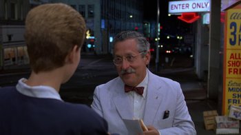 Movie still from “House of Games” (1987), directed by David Mamet – An older man wearing a bow tie talking to a young man; Medium shot, Over the shoulder angle