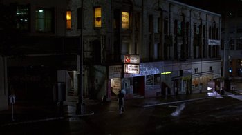 Movie still from “House of Games” (1987), directed by David Mamet – A person riding a bike down a street at night; Extreme Wide shot, High angle